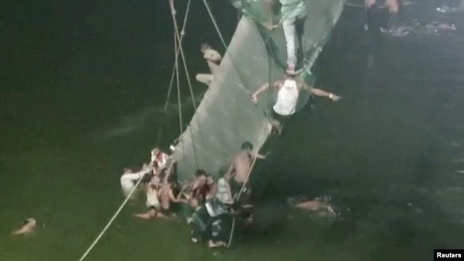 Un grupo de personas se aferran a un puente colapsado en el poblado indio de Morbi el 30 de noviembre de 2022. / Foto: Reuters.